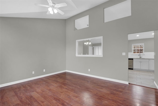 unfurnished living room featuring baseboards, light wood-style flooring, a high ceiling, a sink, and ceiling fan with notable chandelier