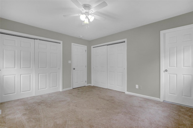 unfurnished bedroom with multiple closets, ceiling fan, carpet floors, and baseboards