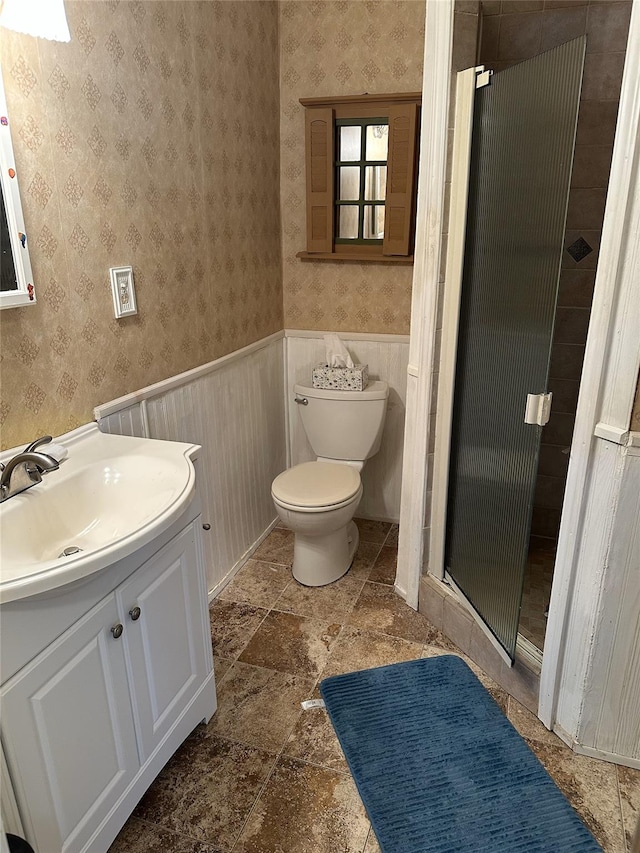 full bath with wainscoting, a shower stall, toilet, and wallpapered walls