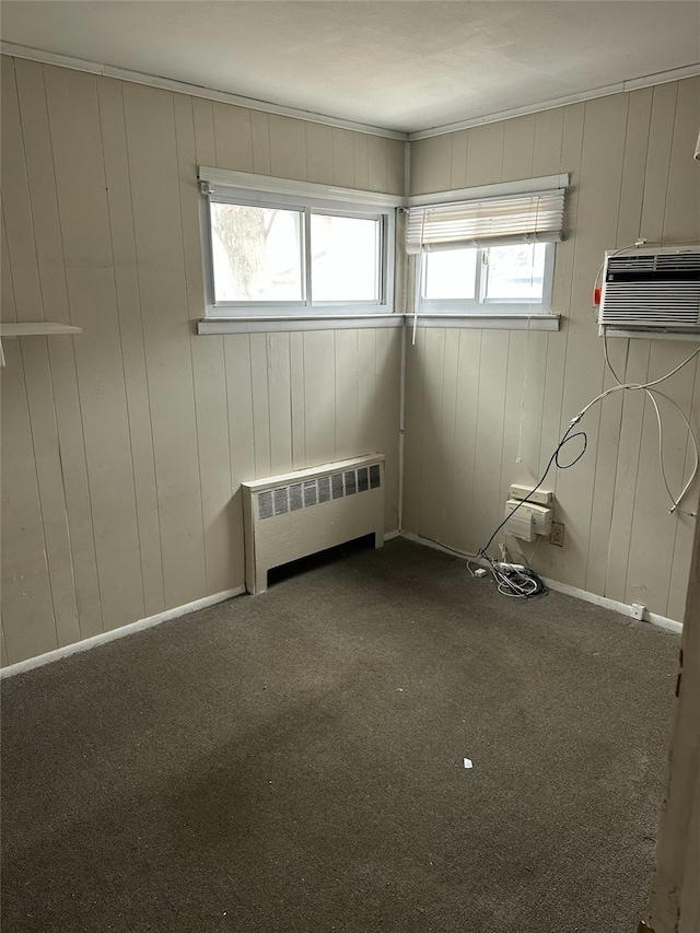 carpeted empty room featuring baseboards, a wall unit AC, and radiator heating unit