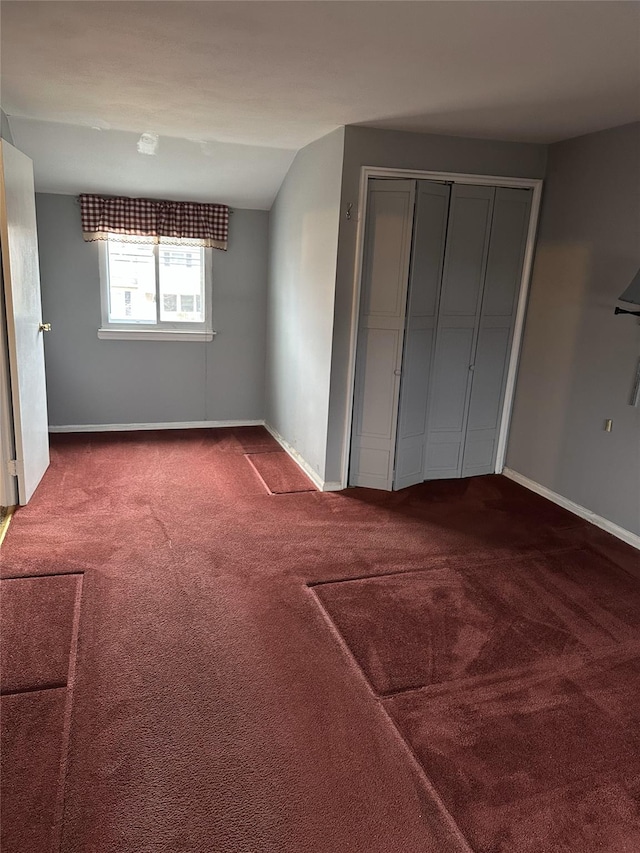 unfurnished bedroom featuring carpet, a closet, vaulted ceiling, and baseboards