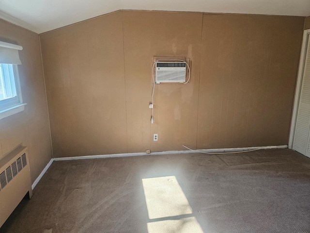 spare room featuring lofted ceiling, a wall mounted air conditioner, carpet flooring, and radiator