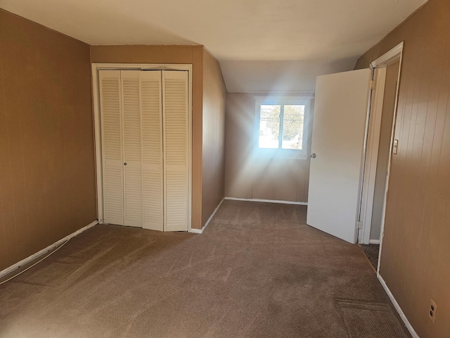 unfurnished bedroom featuring a closet, dark carpet, wood walls, and baseboards