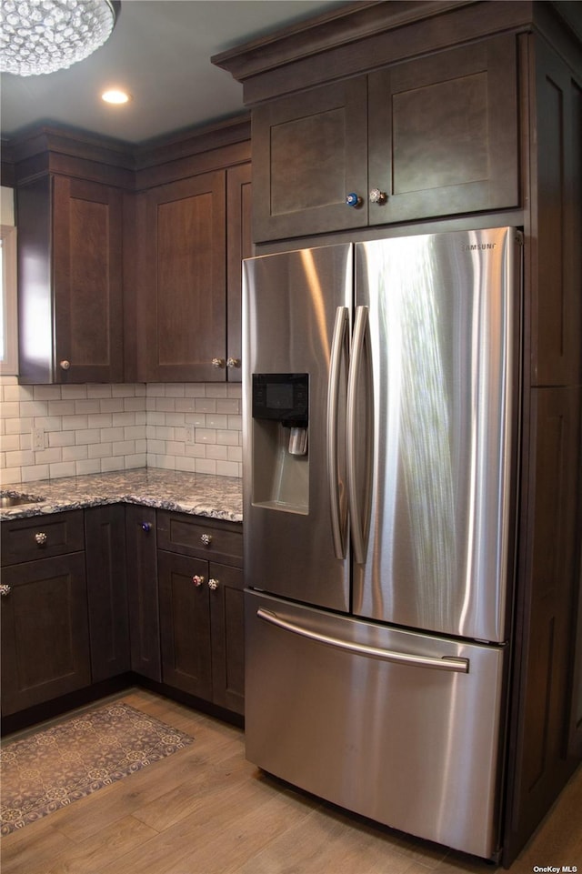 74 Wisconsin St, Long Beach, NY 11561 - kitchen with dark brown cabinets, tasteful backsplash, light stone countertops, light wood-style flooring, and stainless steel refrigerator with ice dispenser
