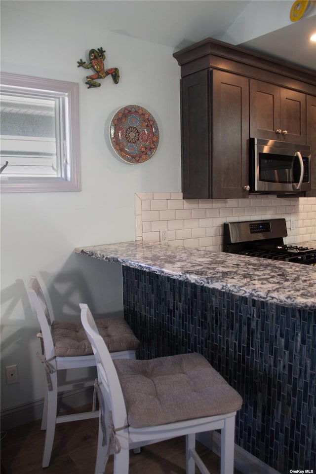 74 Wisconsin St, Long Beach, NY 11561 - kitchen featuring tasteful backsplash, baseboards, dark brown cabinetry, light stone countertops, and appliances with stainless steel finishes