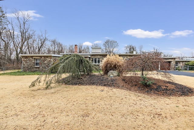 view of front of house with concrete driveway, a chimney, stone siding, and fence