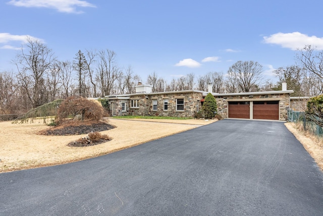 view of front facade with a garage, stone siding, driveway, and a chimney