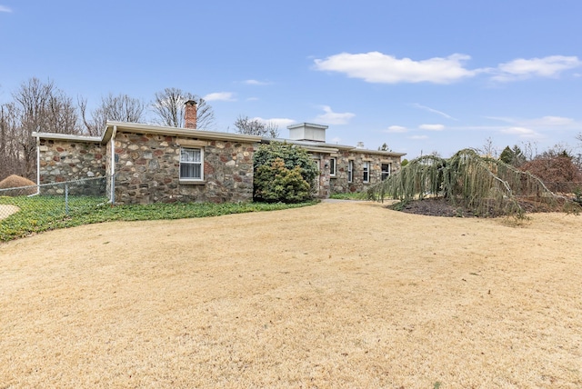 exterior space with stone siding, a chimney, and fence