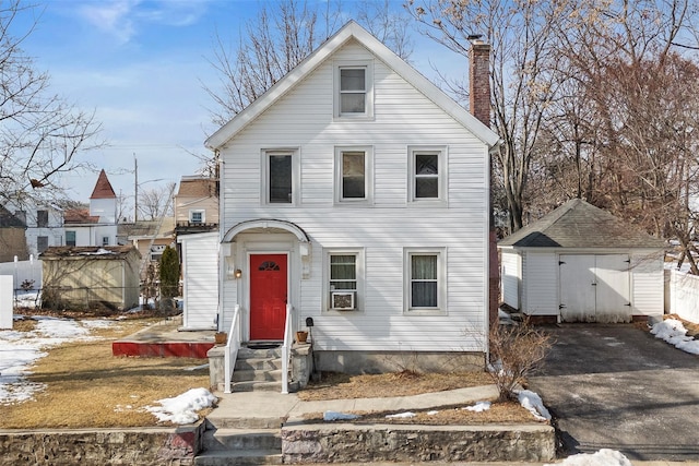 view of front of home featuring aphalt driveway, an outdoor structure, fence, a shed, and a chimney