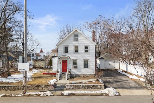 traditional-style home with driveway, a chimney, an outdoor structure, and fence