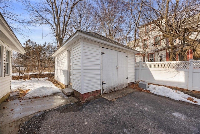 snow covered structure featuring a shed, an outdoor structure, and fence