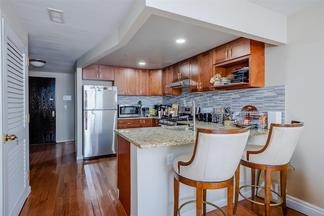 kitchen with visible vents, a peninsula, stainless steel appliances, decorative backsplash, and under cabinet range hood