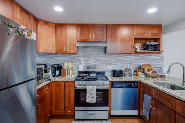 kitchen featuring under cabinet range hood, a sink, stainless steel appliances, decorative backsplash, and light stone countertops