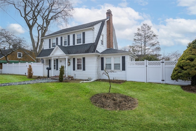 colonial inspired home featuring a front lawn, roof with shingles, a chimney, and fence private yard