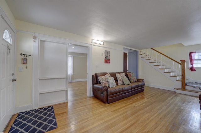 living area featuring light wood-style floors, baseboards, and stairway