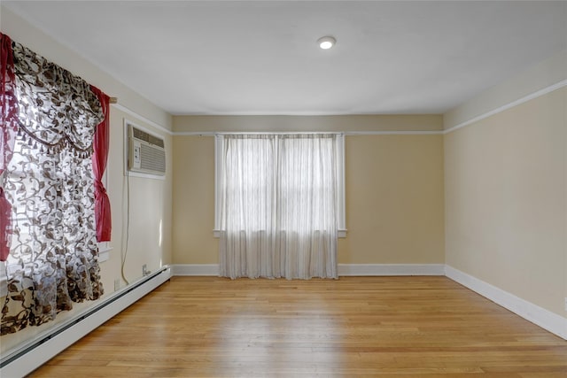 empty room featuring a wall unit AC, a baseboard radiator, baseboards, and light wood-style flooring