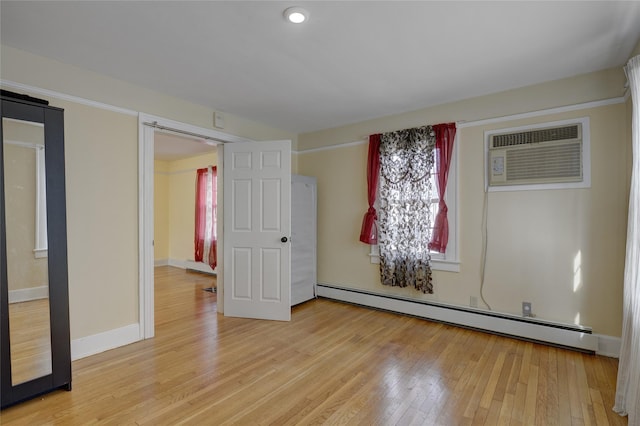 unfurnished room featuring a barn door, baseboards, a wall unit AC, light wood-style floors, and a baseboard heating unit