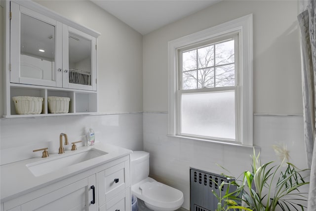 bathroom featuring toilet, radiator heating unit, vanity, and tile walls