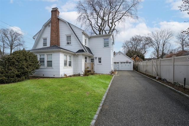 view of front of home with a gambrel roof, a chimney, fence, an outdoor structure, and a front yard