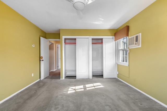 unfurnished bedroom featuring baseboards, a wall mounted AC, carpet flooring, and multiple closets