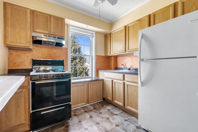 kitchen with tile counters, black range with gas stovetop, ornamental molding, freestanding refrigerator, and under cabinet range hood