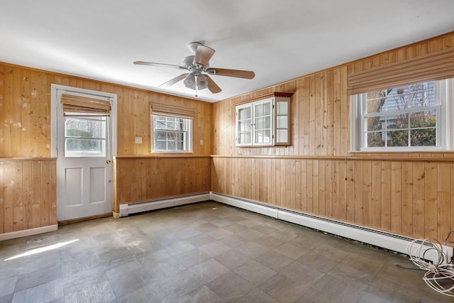 empty room featuring a ceiling fan, wooden walls, baseboard heating, and tile patterned floors