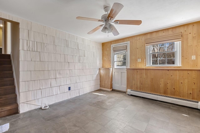 unfurnished room with a baseboard radiator, stairway, wood walls, ceiling fan, and tile patterned floors