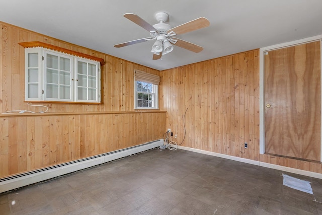 empty room featuring wooden walls, baseboards, ceiling fan, dark floors, and a baseboard heating unit