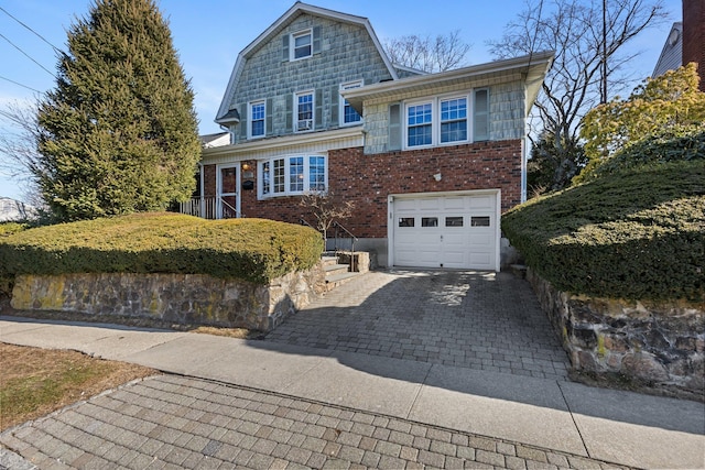 view of front facade featuring a garage, brick siding, decorative driveway, and a gambrel roof