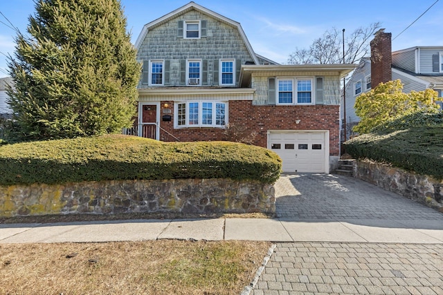 view of front of home featuring decorative driveway, brick siding, an attached garage, and a gambrel roof