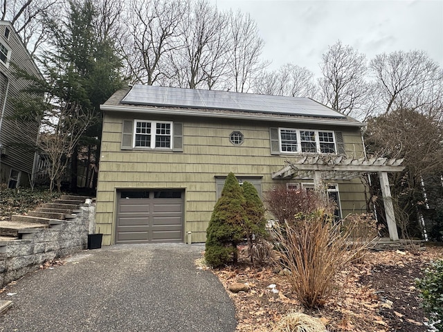 view of front of home featuring an attached garage, driveway, roof mounted solar panels, and a pergola