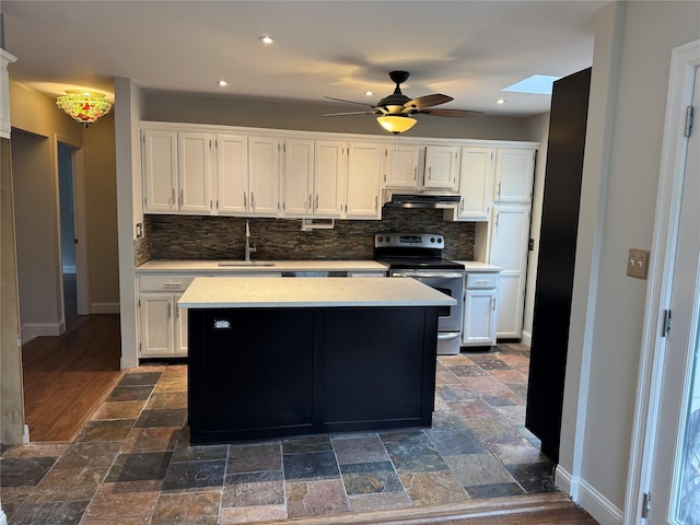 kitchen featuring under cabinet range hood, a sink, white cabinetry, stone finish floor, and stainless steel range with electric stovetop