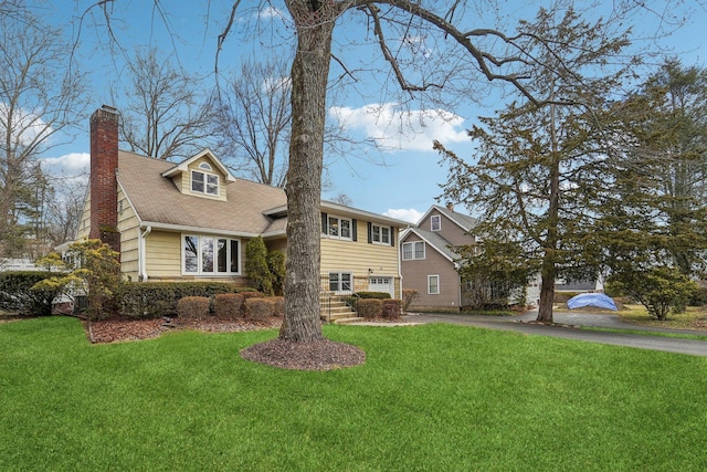 view of front of home with aphalt driveway, a front yard, a chimney, and a garage