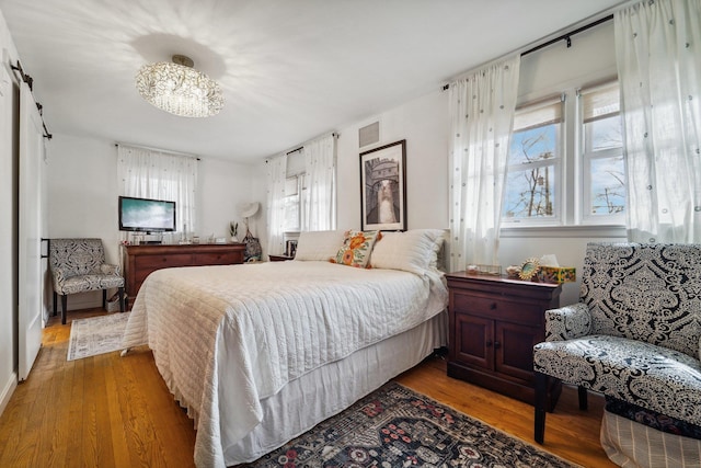 bedroom featuring a barn door, visible vents, and wood finished floors