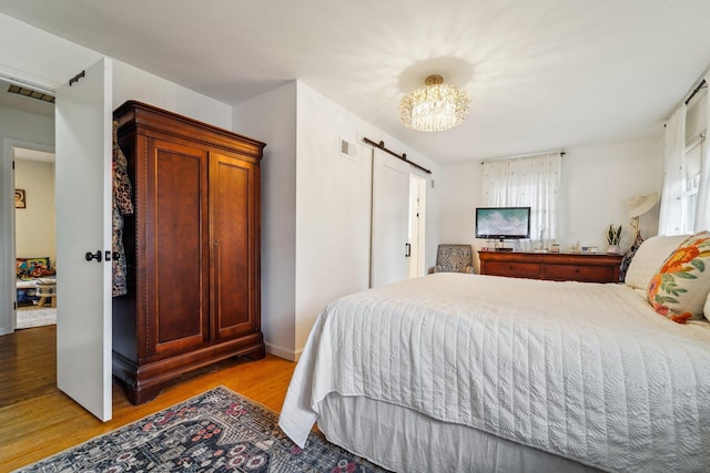 bedroom with a barn door, visible vents, and light wood-style floors