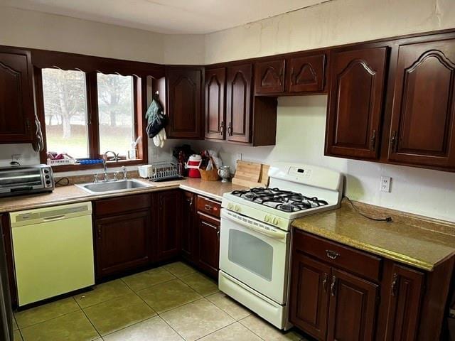 kitchen featuring white appliances, a toaster, light tile patterned floors, dark brown cabinets, and a sink