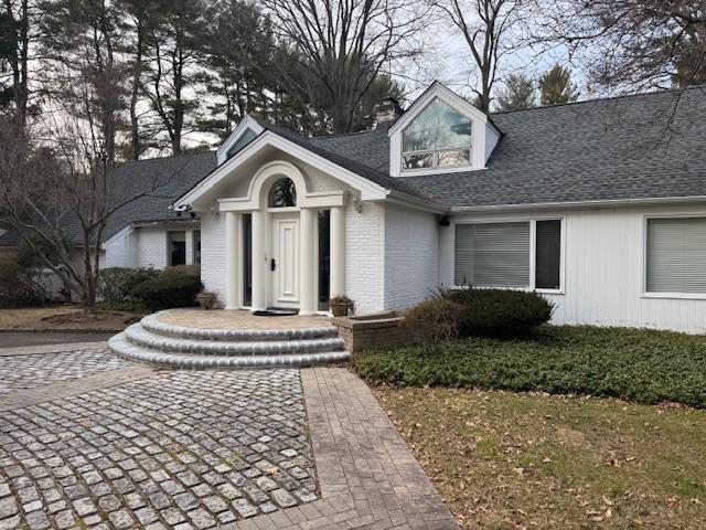 view of front of house featuring roof with shingles, a chimney, and brick siding