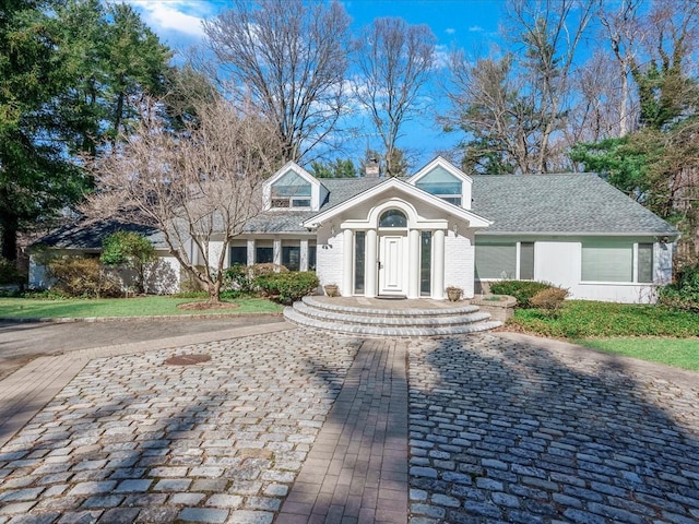 cape cod house featuring brick siding, roof with shingles, and a chimney