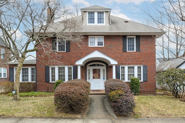 view of front facade featuring brick siding, a front lawn, and roof with shingles