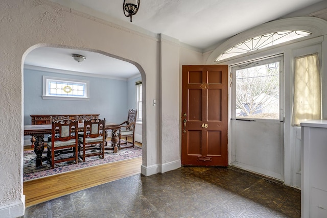 foyer featuring a textured wall, baseboards, arched walkways, and ornamental molding