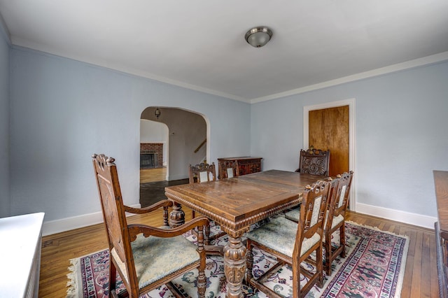 dining room featuring arched walkways, a brick fireplace, hardwood / wood-style floors, and baseboards