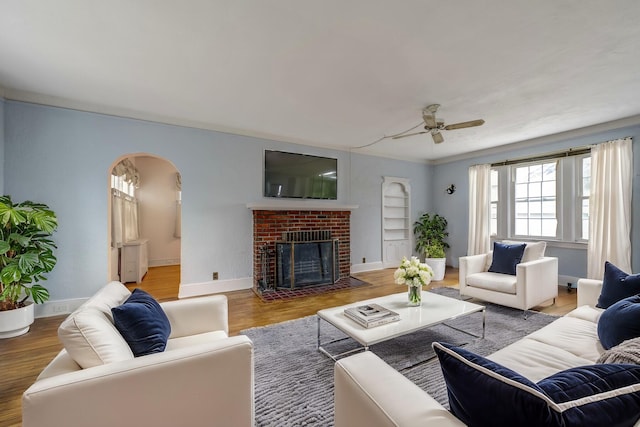 living area with arched walkways, a brick fireplace, baseboards, and wood finished floors