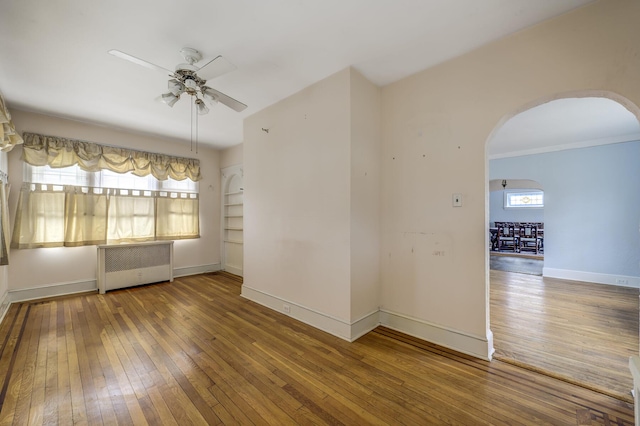 unfurnished room with arched walkways, plenty of natural light, radiator heating unit, and hardwood / wood-style flooring