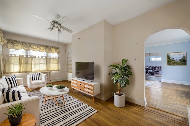 living room with arched walkways, ceiling fan, built in shelves, wood finished floors, and baseboards