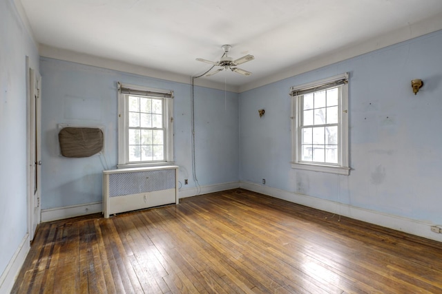 spare room with radiator heating unit, wood-type flooring, a ceiling fan, and baseboards