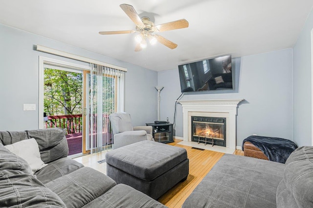 living room featuring light wood-style floors, a fireplace with flush hearth, and a ceiling fan