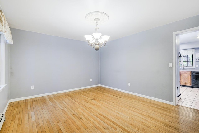 spare room featuring a baseboard radiator, light wood-style flooring, baseboards, and an inviting chandelier