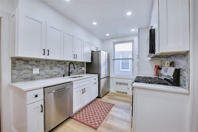 kitchen with appliances with stainless steel finishes, white cabinetry, a sink, and radiator heating unit