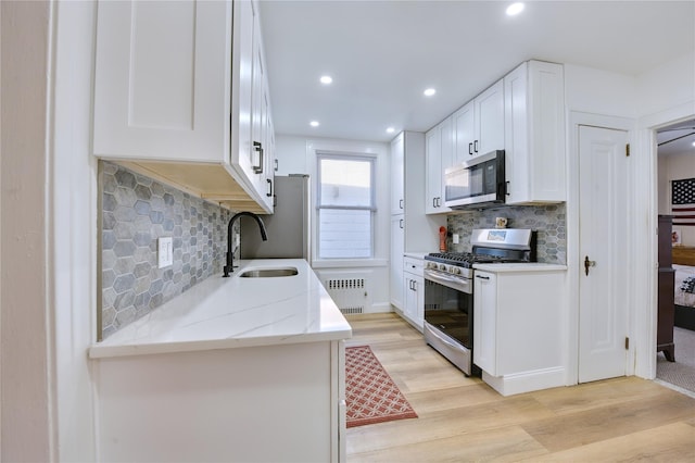 kitchen featuring stainless steel appliances, a sink, white cabinets, light wood-type flooring, and radiator heating unit