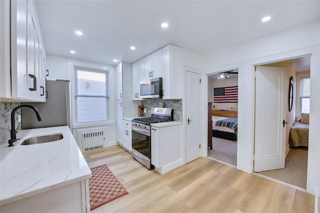 kitchen with stainless steel appliances, radiator heating unit, light wood-style floors, white cabinets, and a sink